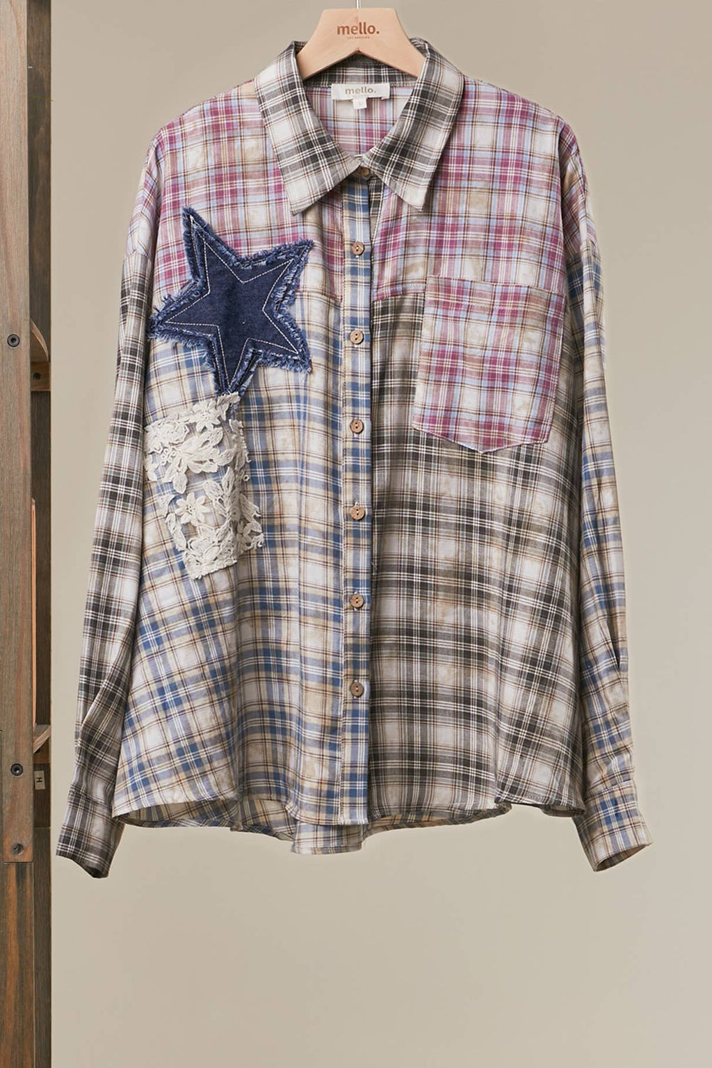 A long-sleeve plaid button-up shirt hanging on a wooden hanger, featuring a blue denim star patch and a lace applique pocket on the left side. The shirt has a beige, blue, and pink plaid pattern with brown buttons.