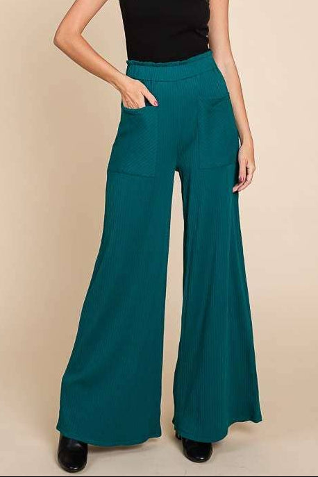 Woman wearing teal wide-leg pants and a black top against a beige background