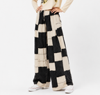 A person wearing wide-leg patchwork pants with large black and cream blocks, paired with a cream sweatshirt and white sneakers, photographed against a plain light gray studio background.