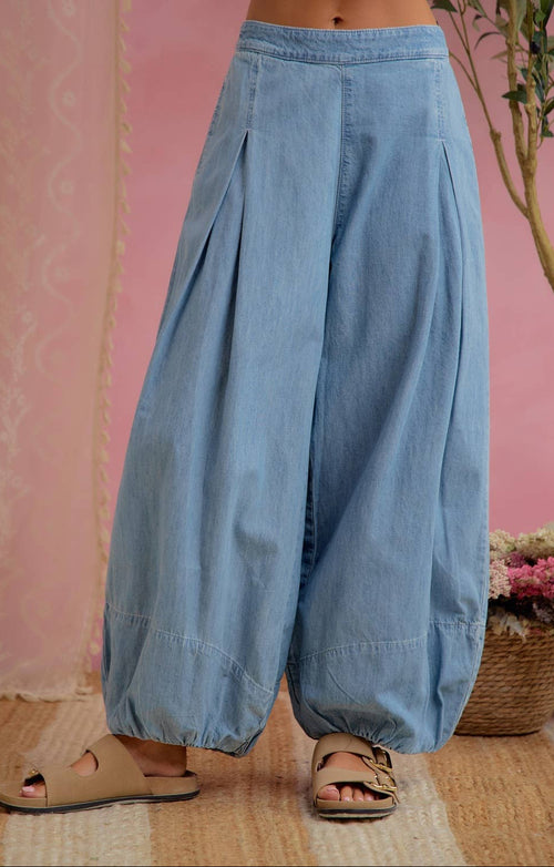 Light blue wide-leg harem pants with a drawstring waist and gathered cuffs, shown on a model wearing beige slide sandals against a pink wall backdrop.