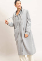 A woman modeling a light gray hooded longline cardigan or coat with a front zipper, shown against a plain light beige studio background.