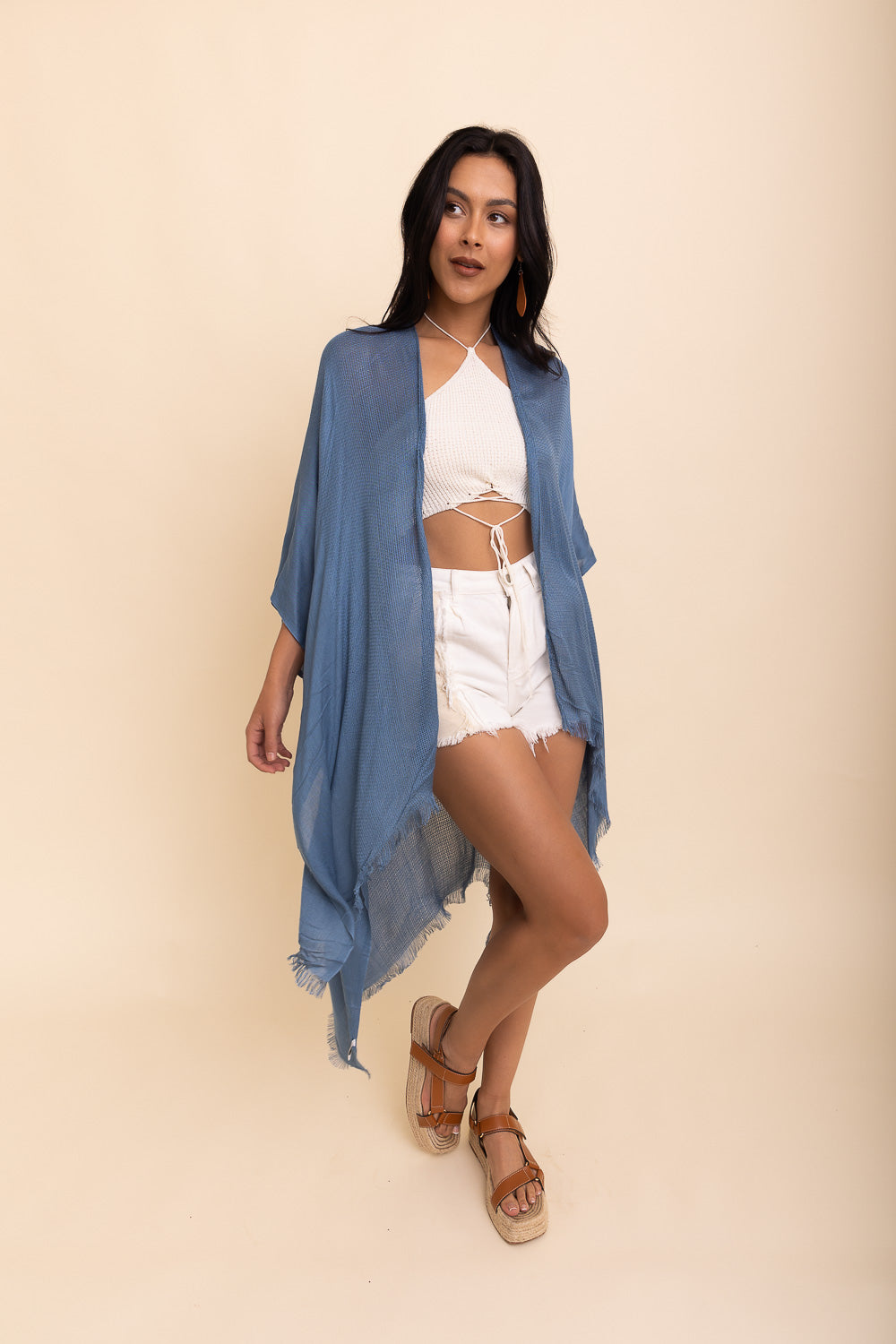 A woman wearing a blue frayed trim kimono with white shorts and a white top, standing against a neutral background.